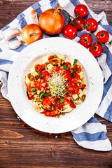 Pasta with tomato sauce and vegetables on wooden table