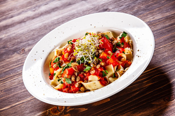 Pasta with tomato sauce and vegetables on wooden table