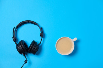 Music or podcast background with headphones and cup of coffee on blue table, flat lay. Top view, flat lay