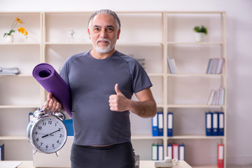 White bearded old man employee doing exercises in the office