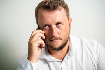 serious male in a white shirt talking on the phone on a white gray background
