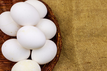 White chicken eggs in wicker basket on sackcloth background