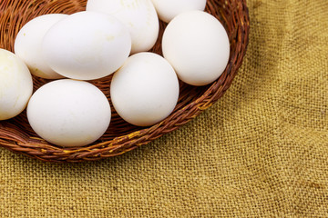 White chicken eggs in wicker basket on sackcloth background