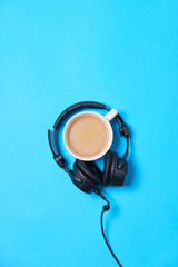 Music or podcast background with headphones and cup of coffee on blue table, flat lay. Top view,...