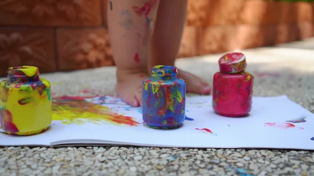 child legs draws a finger paint - blue, red and yellow on a white sheet of paper. Creative child development in kindergarten or free time at home. slow motion