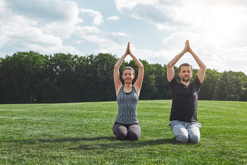 Morning time. Woman and man meditating together outdoors while sitting on a green lawn in open field. Yoga concept.