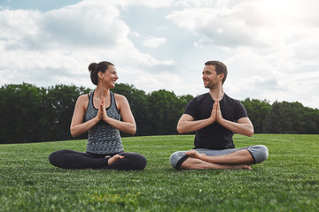 Yoga in pair. Happy couple practicing meditation exercises outdoors and looking at each other with...