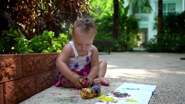 Beautiful little girl draws with finger paints on a white sheet of paper. Creative child development in kindergarten or free time at home. slow motion.