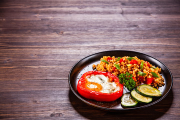 Fried egg, groats and vegetables on wooden table