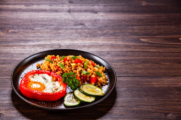 Fried egg, groats and vegetables on wooden table