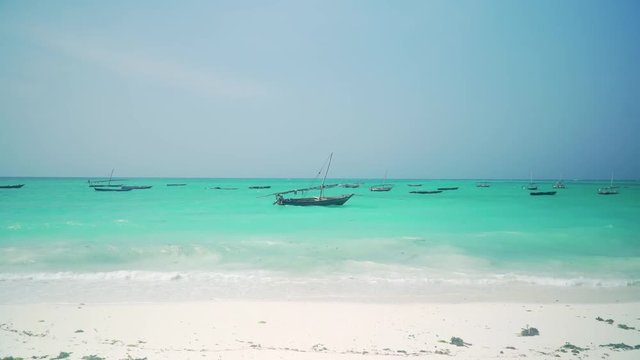 Traditional African wooden dhow boat swing on the waves of bright turquoise ocean near sandy coast on sunny day. Nungwi and Kendwa beach, Zanzibar, Tanzania, Africa.