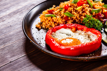 Fried egg, groats and vegetables on wooden table