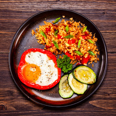 Fried egg, groats and vegetables on wooden table