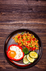 Fried egg, groats and vegetables on wooden table
