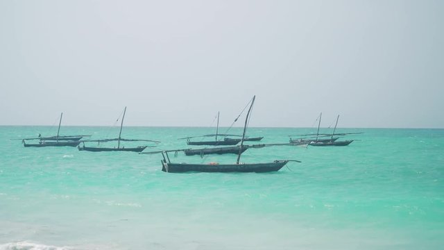 Traditional African wooden dhow sailing boats bobs and swing on the waves of bright turquoise ocean on sunny day. Zanzibar, Tanzania, Africa.
