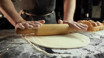 Chef in a black apron rolling dough with flour using a rolling pin side view