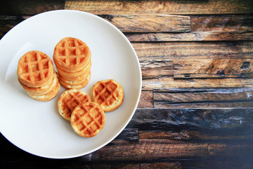 small round baked waffles in a white deep plate on a brown wooden background