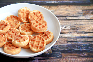round waffles in a white plate on a brown wooden background