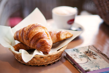 croissants in a wicker plate next to a cup of coffee and a notebook