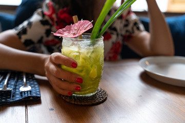 Woman holding tropical green color cocktail in a transparent tiki style cocktail glass