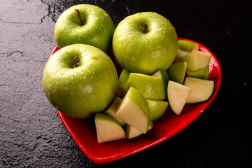 Ripe green apples into heart bowl on table close up.