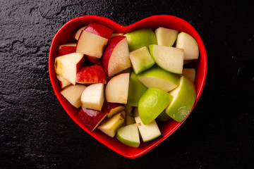 Ripe red and green apples into heart bowl on table close up. © paulovilela
