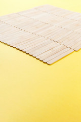 Many wooden ice cream sticks in row on yellow background