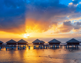 Fototapeta na wymiar Water Bungalows with a idyllic Sunset, beautiful Sky and Clouds in the Lagoon Huahine, French Polynesia. Copy space for text.