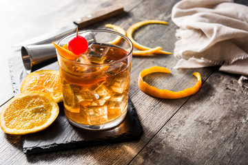 Old fashioned cocktail with orange and cherry on wooden table. Copyspace