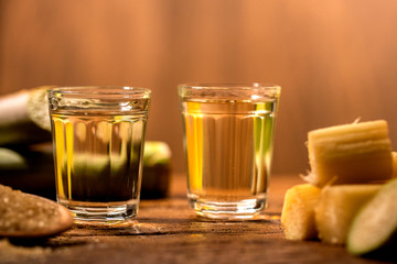two shot glasses of Brazilian gold  cachaca with sugar and sugarcane isolated on rustic wooden background