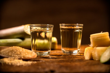 two shot glasses of Brazilian gold  cachaca with sugar and sugarcane isolated on rustic wooden background