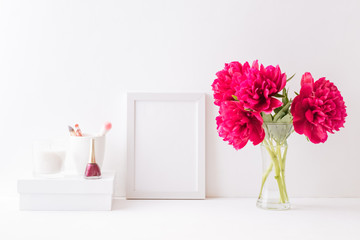 Home interior with decor elements. White frame, red peonies in a vase, cosmetic set