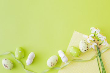 Flat lay composition with white daffodils and easter eggs on a green background