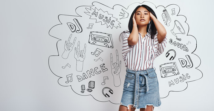 I love music. Beautiful asian woman in casual wear playing with her hair and looking at camera while standing against grey background with music theme doodles