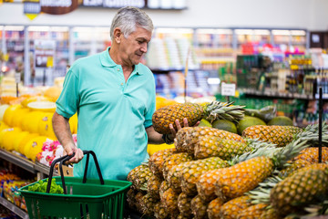 Handsome man posing, looking and holding fruit in hand. Bearded customer smiling. Section with...