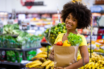 Healthy positive happy african woman holding a paper shopping bag full of fruit and vegetables