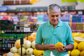 Handsome man posing, looking at camera and holding melon in hand. Bearded customer smiling. Section with fresh citruses on background