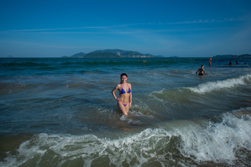 beautiful young woman in a seductive bikini comes out of the sea with high waves. Big waves in the ocean