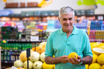 Handsome man posing, looking at camera and holding melon in hand. Bearded customer smiling. Section with fresh citruses on background
