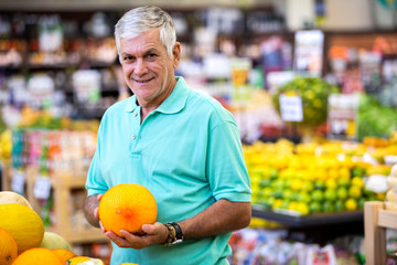 Handsome man posing, looking at camera and holding melon in hand. Bearded customer smiling. Section...