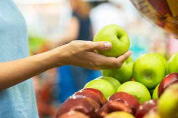 Woman's hand choosing green apple in supermarket