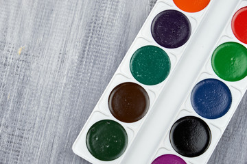 A palette of watercolor paints and brushes of different sizes, lying on a gray wooden background