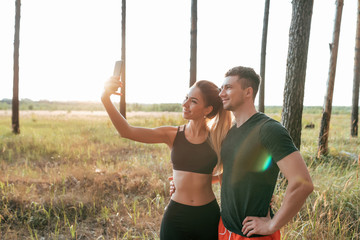 A young couple, a man and a woman, summer park, are photographed on the phone, happy smiling, before jogging, sports activities in the fresh air, active lifestyle. Sportswear emotions joy and fun.