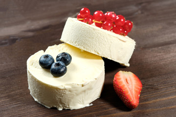 Two white ice cream o with strawberries, blueberries and red currants on the dack wood background