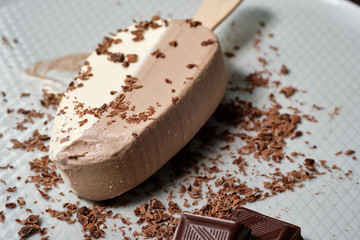 white chocolate ice cream on a stick on a white plate with chocolate chips on the dack wood background