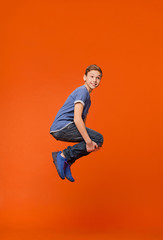 Fototapeta na wymiar Emotional boy jumping in bomb style on orange