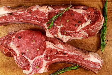 Raw fresh beef rib eye steaks on bone with spices and rosemary on wooden table. Top view