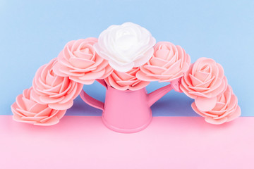pink watering can with artificial roses on a colored background