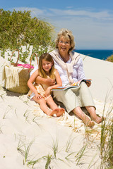 Grand mother and grand daughter reading on the beach