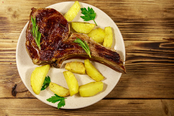 Roasted beef rib eye steak on bone with baked potatoes and herbs on wooden table